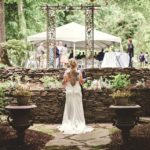 Bride standing looking at guests under tent from a rock garden area