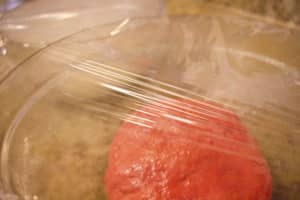 red and white colored dough in two bowls covered in plastic wrap