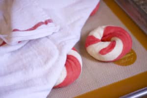 four red and white bagels on a baking sheet covered by a clean, dry tea towel