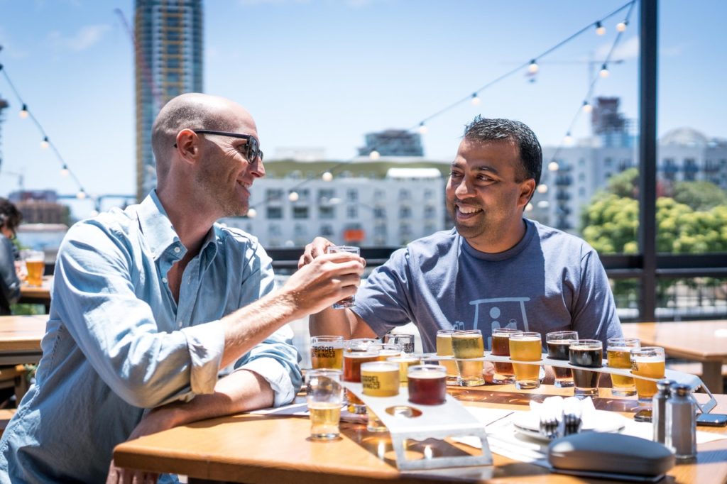 two men sitting outside drinking beer samples