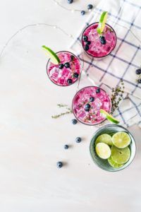 three berry mojito glasses on a table with limes and blueberries