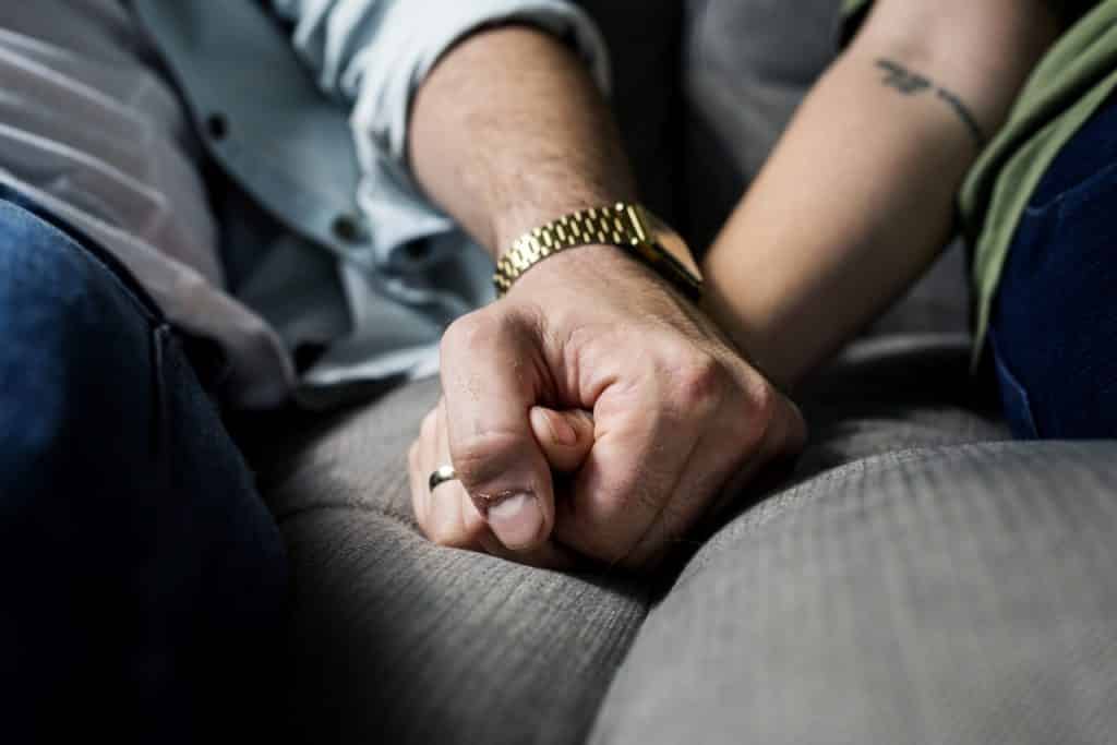 close up of a man and woman's hands clasped while sitting on a grey couch